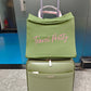 Green suitcase with a green cover labeled 'Travel Pretty' on a marble floor.
