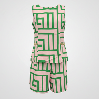 A sleeveless matching set consisting of a peplum top and shorts, featuring a bold green geometric maze-like pattern on a light pink background, displayed against a light gray gradient background.